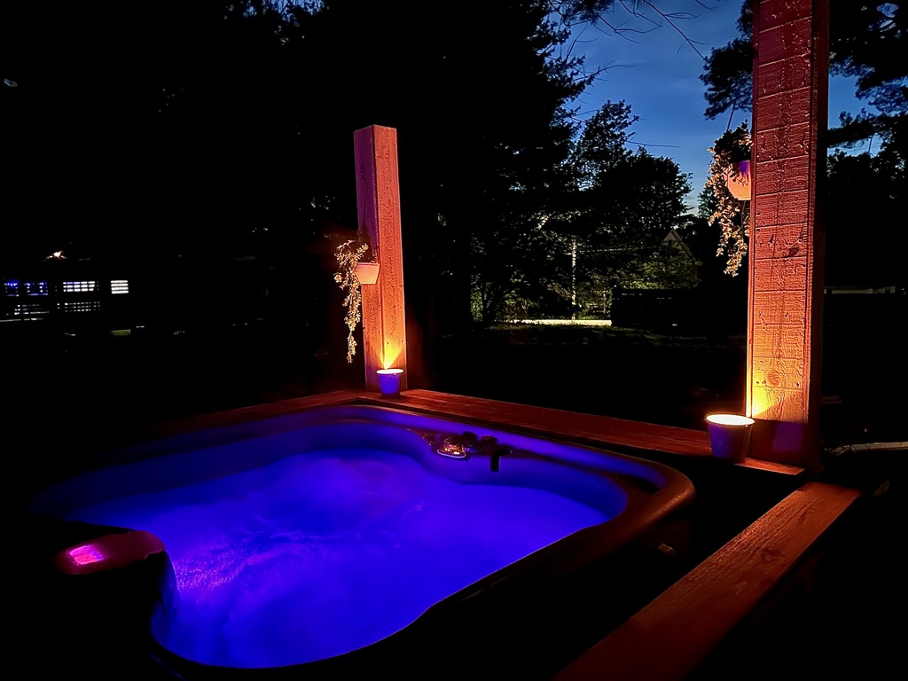 Maple Villa's blue-lit outdoor hot tub beside warmly lit wooden posts at night