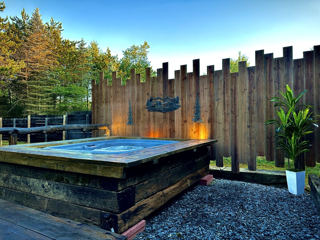 Pin Oak Villa's outdoor hot tub beside a wooden privacy screen and greenery in daylight
